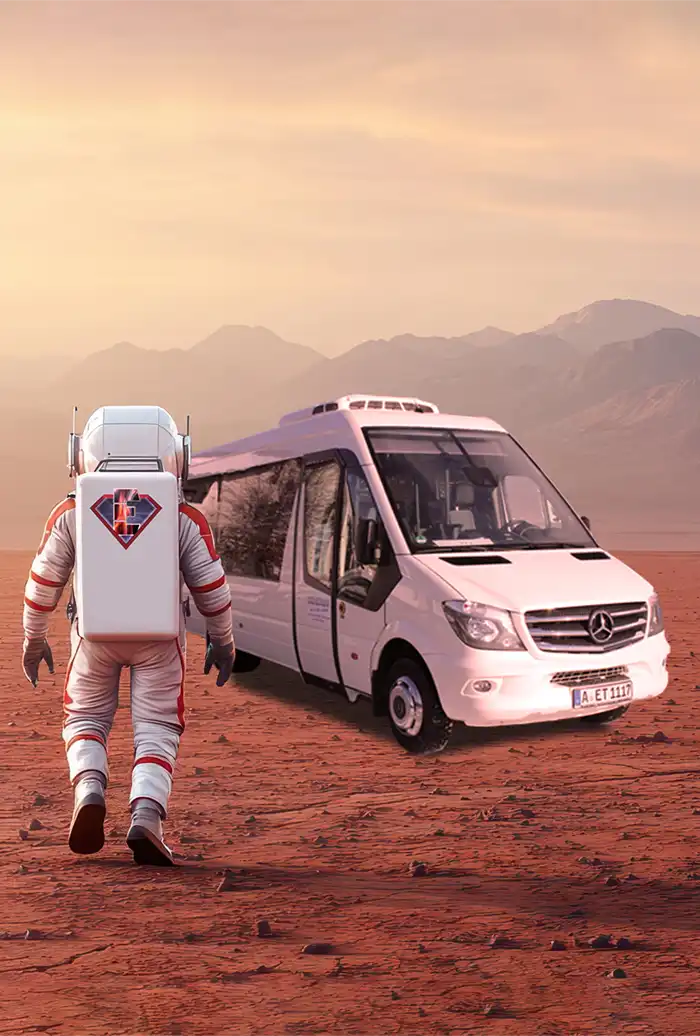 Ein Astronaut nähert sich einem weißen Lieferwagen in einer roten, felsigen Landschaft mit entfernten Bergen.