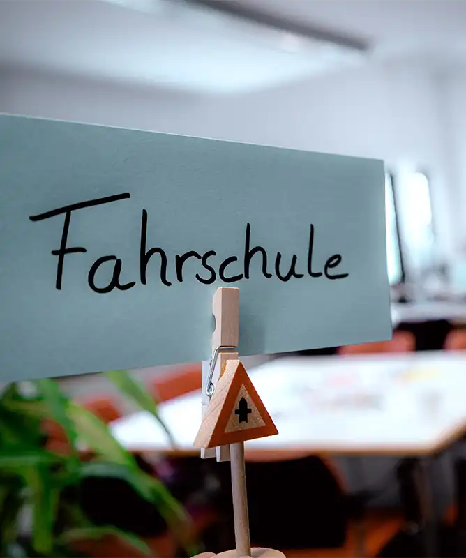 Ein Schild mit der Aufschrift "Fahrschule Egenberger" ist auf einem Ständer in einem Klassenzimmer angebracht.