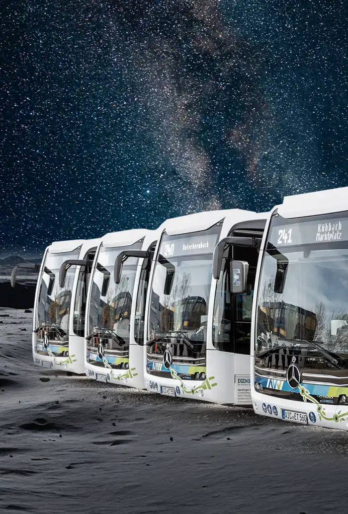 Vier weiße Stadtbusse fahren auf dunklem Sand unter einem Sternenhimmel und der Milchstraße.